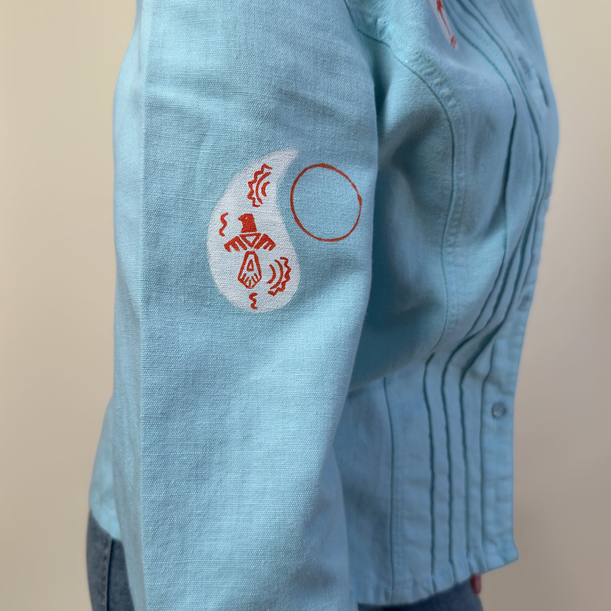 Close-up of hand-painted red and white symbols on the sleeve of Before Borders | Under One Sun by HANDLURIA.