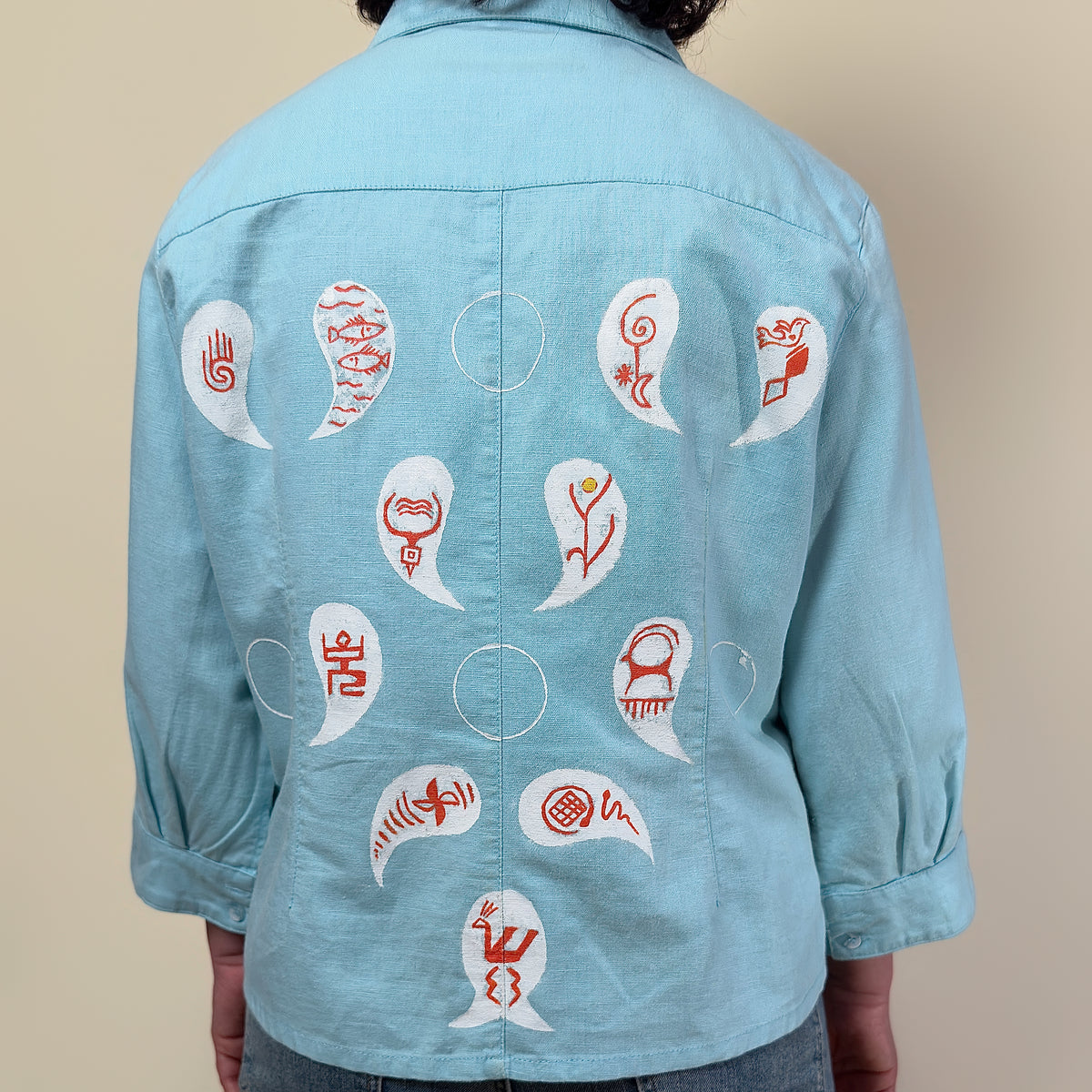 Detail view of Before Borders | Under One Sun by HANDLURIA, showing hand-painted red symbols within white curved shapes across the back.