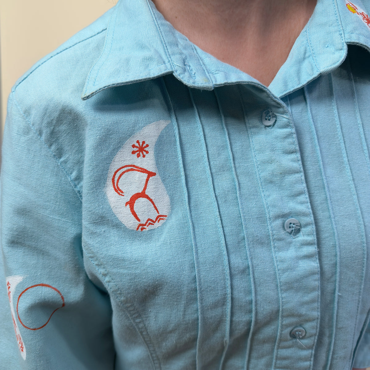Detail view of Before Borders | Under One Sun by HANDLURIA, showing the collar, pleated front and hand-painted red and white symbols.
