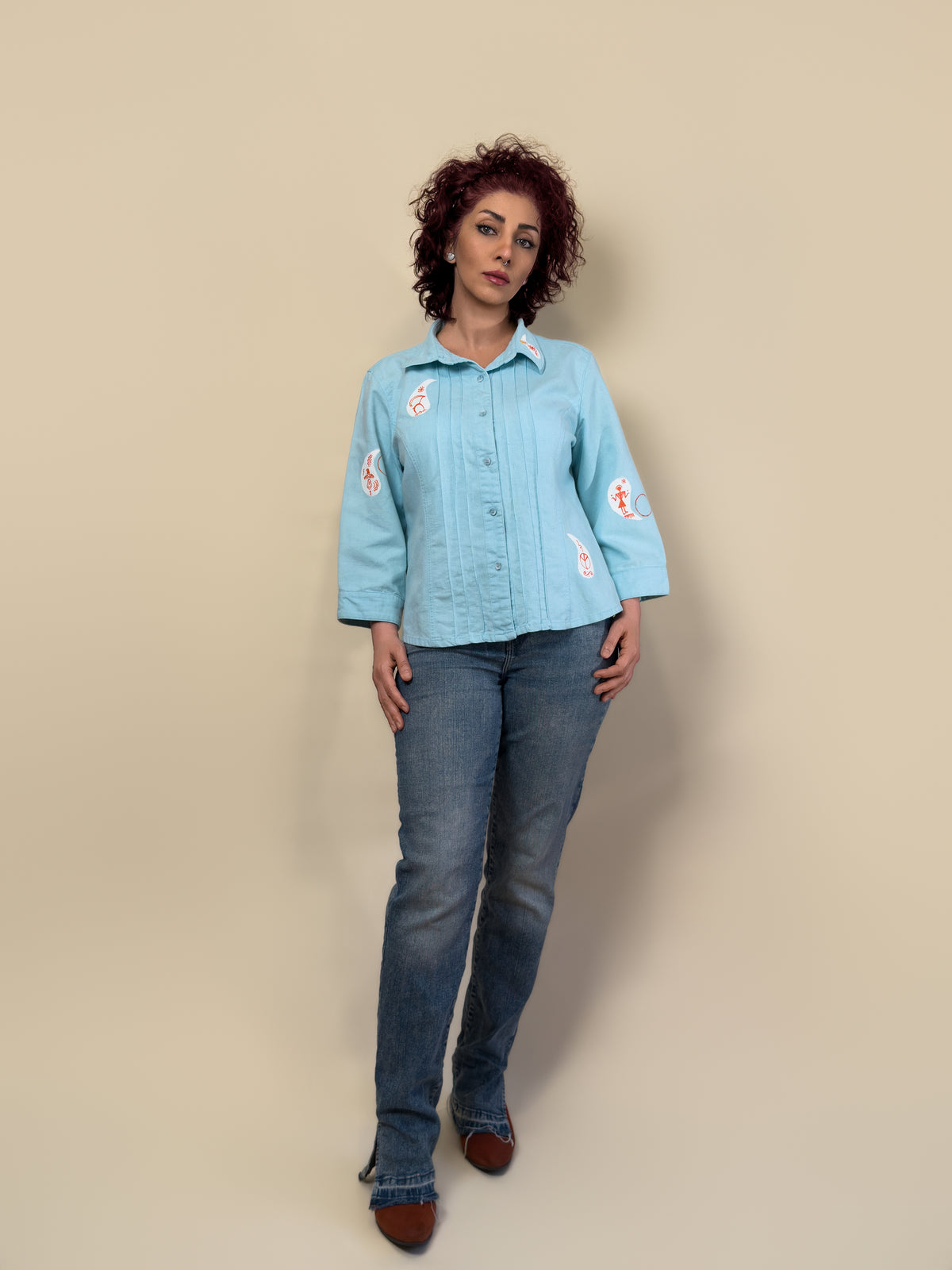 Front view of the Before Borders | Under One Sun turquoise shirt jacket by HANDLURIA, featuring hand-painted white and red symbols.