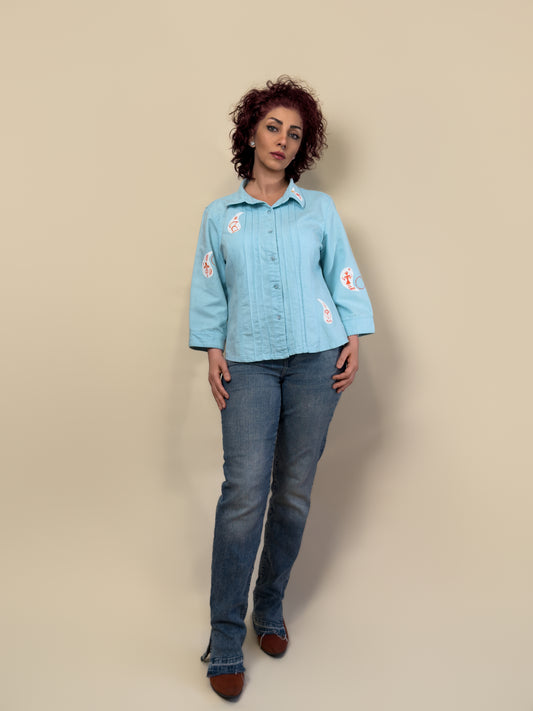 Front view of the Before Borders | Under One Sun turquoise shirt jacket by HANDLURIA, featuring hand-painted white and red symbols.