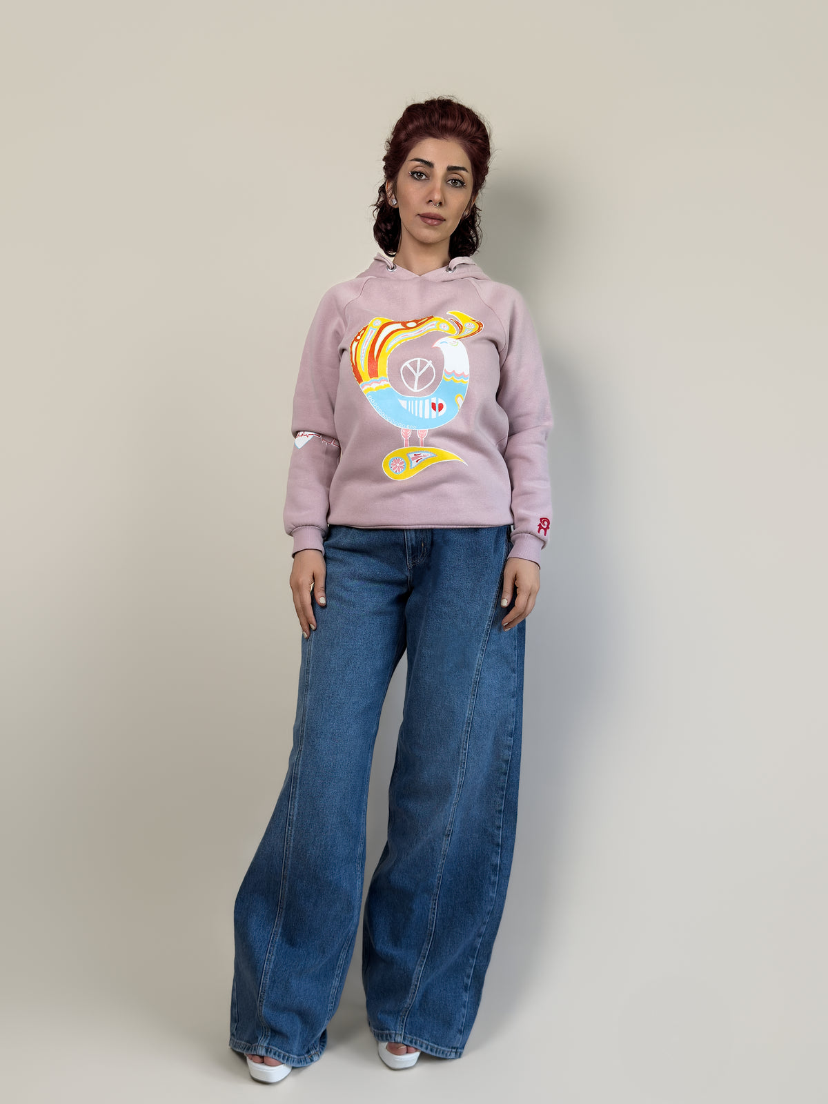 Front view of the Northern Bird Song | Painted blush-pink hoodie by HANDLURIA, featuring a colorful hand-painted bird motif.