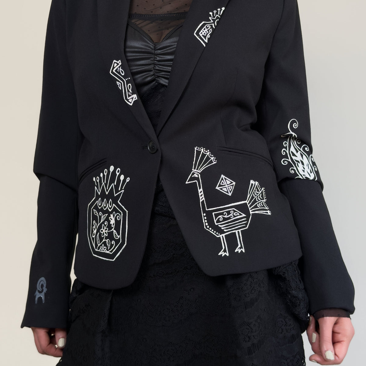 Close-up of HANDLURIA's Peace Tide black blazer featuring white hand-painted bird, crest, and ornamental motifs.
