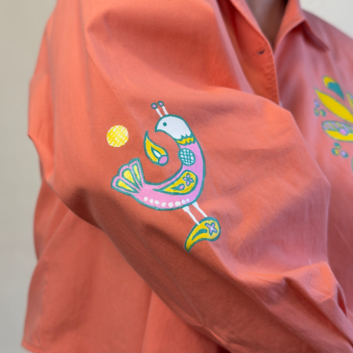 Close-up of the hand-painted pink, teal and yellow bird on the sleeve of Songbird Bloom by HANDLURIA.
