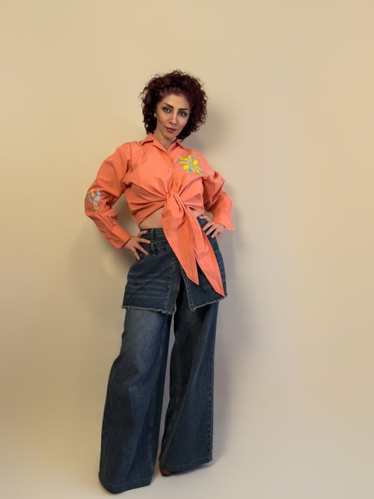 Front view of the Songbird Bloom coral tie-front shirt by HANDLURIA, featuring a hand-painted flower motif and bird on the sleeve.